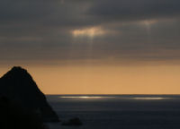 雲見の烏帽子山の先で雲の間から太陽が射し込み海が部分的に光っています